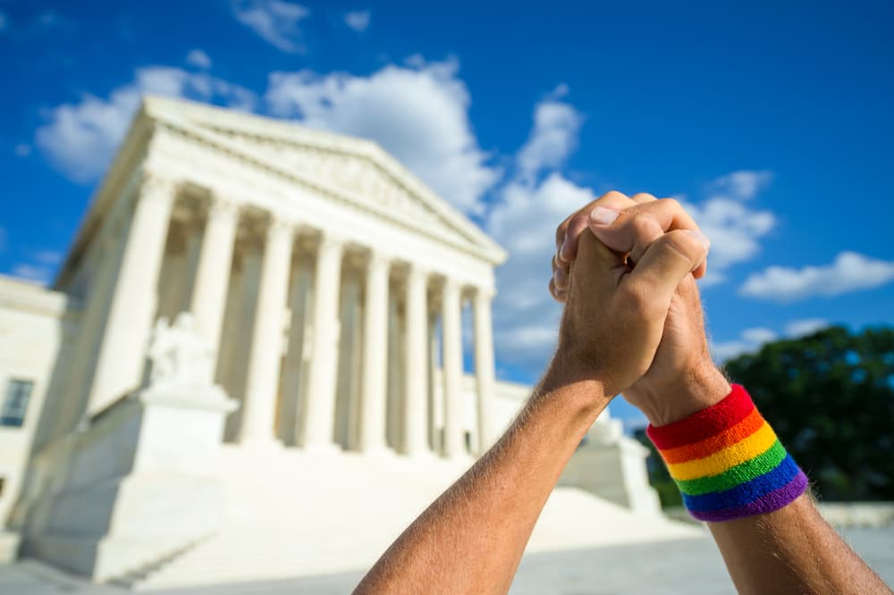 Hands clasped in prayer wearing a rainbow pride wristband outside the Supreme Court building.