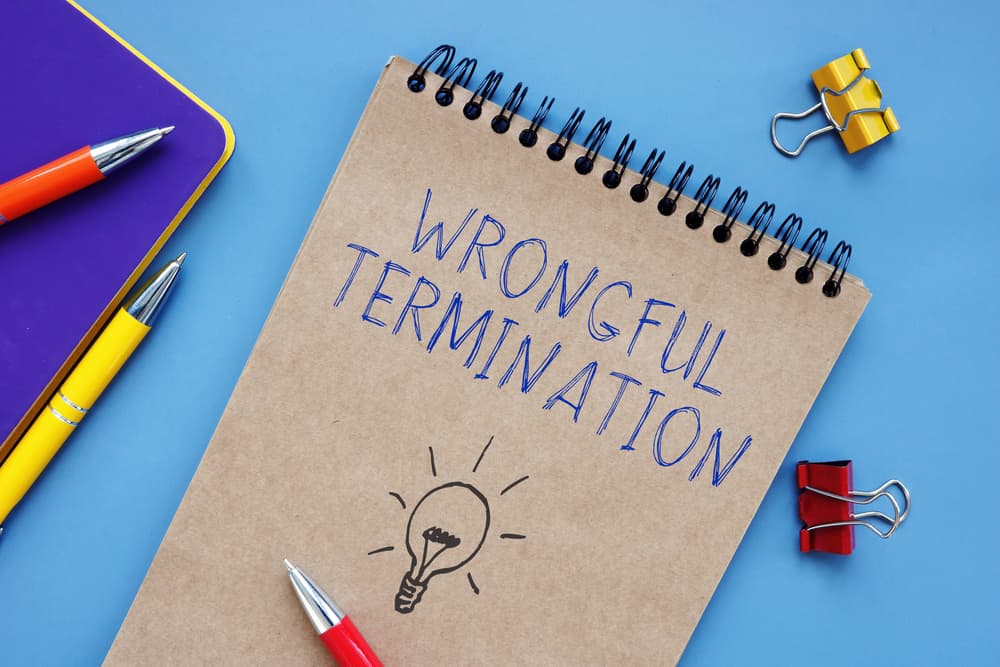 Notepad with "Wrongful Termination" written on it, pens, clips, and a tablet on a blue background.