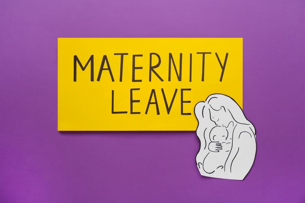 Maternity leave concept symbolized by a note with a paper cutout of a mother and child , presented in a top-down perspective.