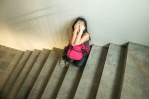Student sitting on stairs, hands covering face. Illustrates the issue of Sexual Harassment in campus
