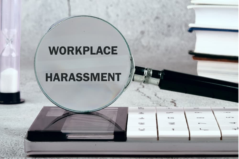 WORKPLACE HARASSMENT written on the background through a magnifying glass.