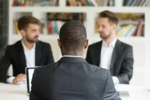 Rear view at african businessman against two caucasian men wearing suits, black vacancy candidate sitting his back to camera on job interview with two employers