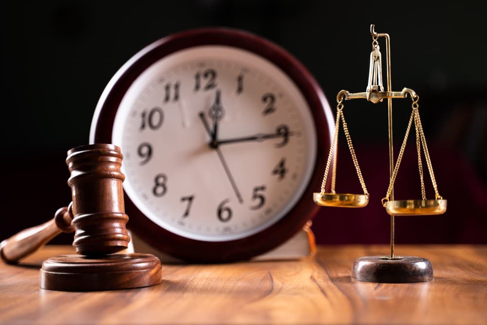 Wooden gavel and justice scales on a table with a clock in the background