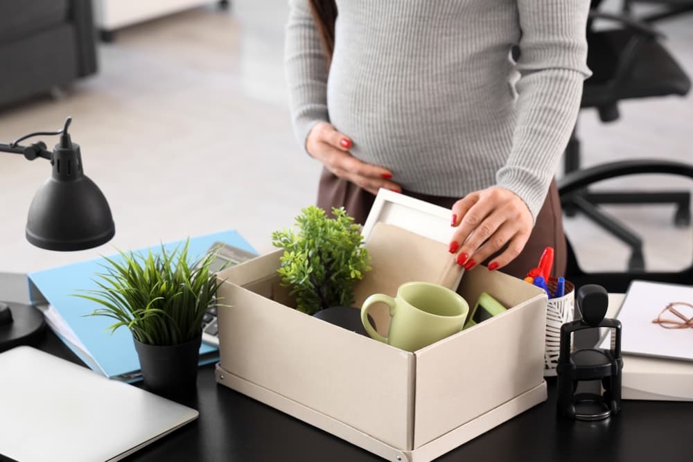 Fired or wrongfully terminated pregnant businesswoman packing personal stuff in office