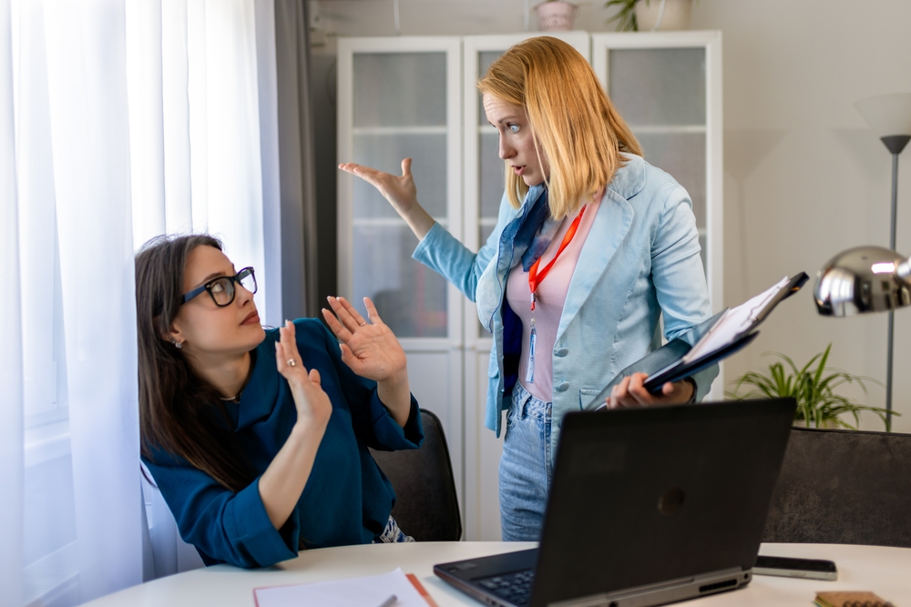 A woman yelling at another woman in an office setting, depicting a tense and hostile work environment.